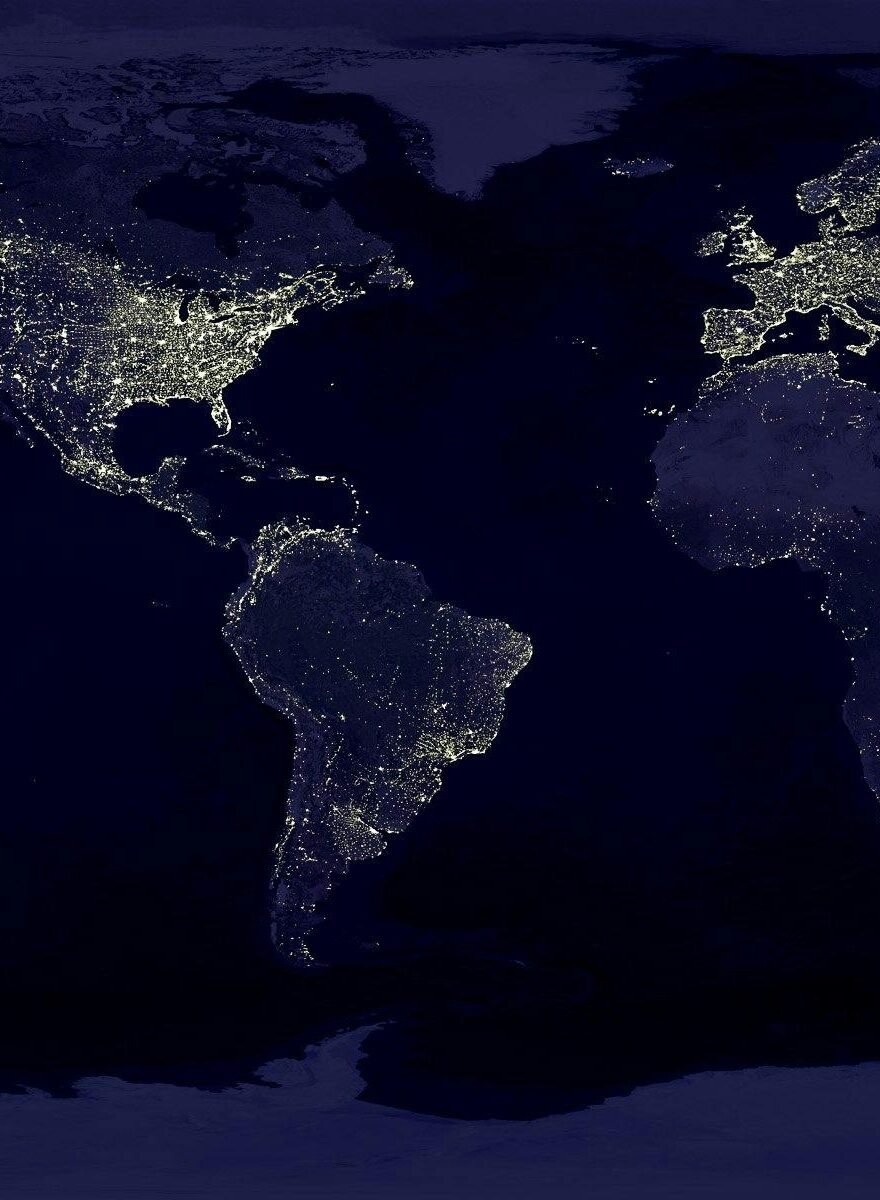 Satellite view of Earth at night with illuminated cities across continents.